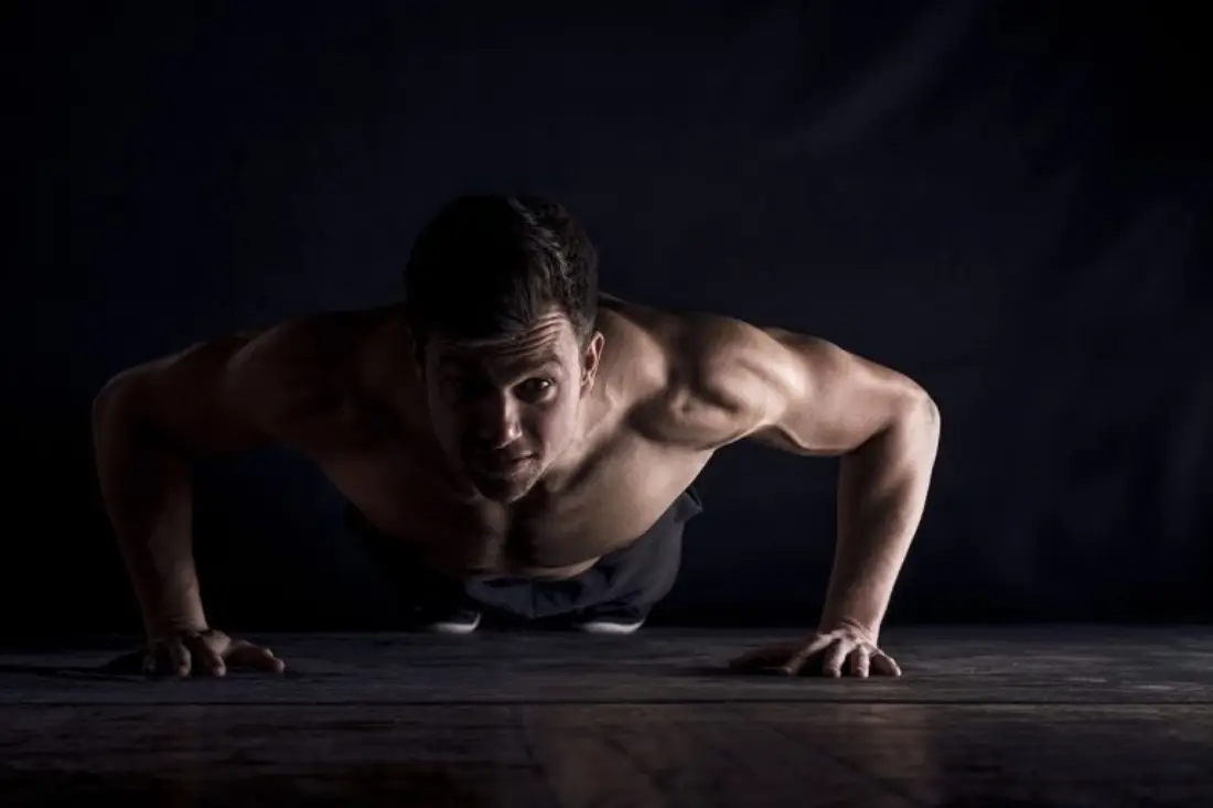 Homem sem camisa com músculos definidos fazendo flexão no chão.