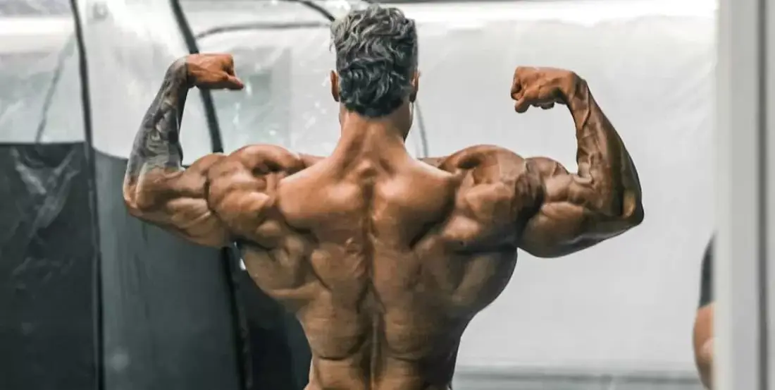 CBUM, campeão do Mister Olympia de costas fazendo pose muscular.