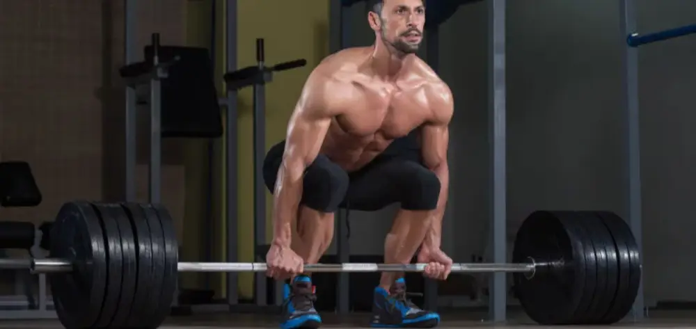 Homem fazendo levantamento terra com barra e com anilhas do chão na academia.