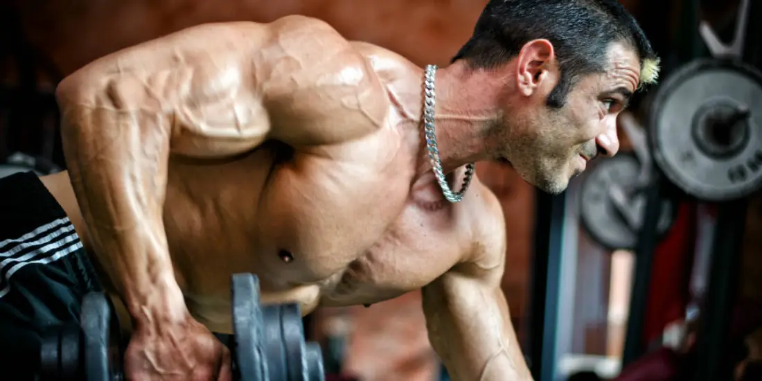 Homem sem camisa com musculos bem definidos fazendo exercício de coice para tríceps.