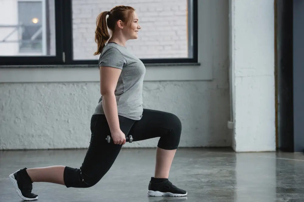 Mulher fazendo afundo com halteres na academia em busca de treino nos glúteos.