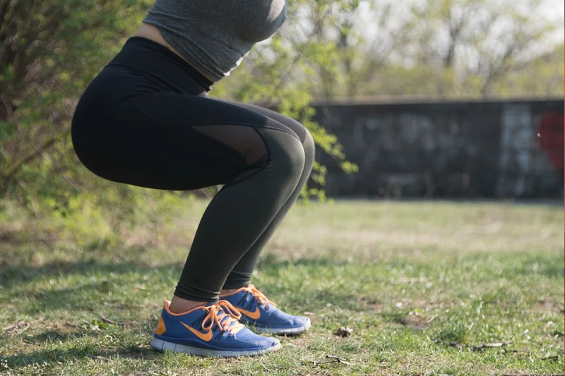 Mulher fazendo agachamento ao ar livre para ter os benefícios do emagrecimento que o exercício traz