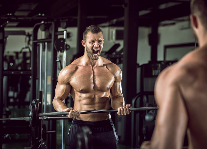 Homem na academia mostrando como fazer o treino de rosca direta